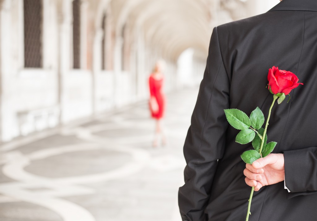 Man waiting for his date with red rose behind his back